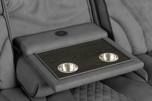 Detalle de consola central integrada en sofá reclinable gris oscuro, con bandeja de acabado tipo madera, dos portavasos metálicos y cargador inalámbrico incorporado. Diseño funcional para entretenimiento y comodidad en el hogar.