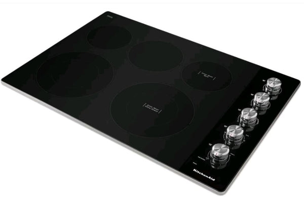 Tope KitchenAid con superficie vitrocerámica negra, cinco zonas de cocción eléctricas y controles giratorios metálicos laterales. Diseño elegante y moderno para cocinas contemporáneas con instalación integrada.
