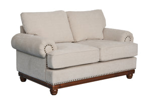 Loveseat clásico tapizado en tela beige clara, con cojines acolchados, apoyabrazos enrollados, detalles de tachuelas metálicas y base de madera oscura sobre fondo blanco.