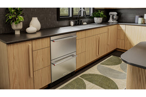 Una nevera empotrada de acero inoxidable instalado en una cocina moderna con armarios de madera clara, encimeras oscuras y una alfombra estampada en verde y beige.