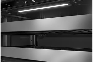 Primer plano de la nevera de vinos empotrada de acero inoxidable, con una pantalla de control digital en la parte superior, una luz brillante debajo del mueble y compartimentos interiores oscuros.