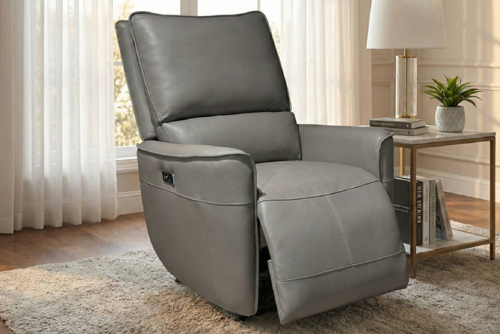 Butaca reclinable individual tapizado en material sintético color gris, con respaldo alto acolchado, apoyabrazos anchos y reposapiés extendido. Incluye un control lateral integrado en uno de los lados del asiento. Diseño cómodo y moderno, presentado sobre fondo blanco.