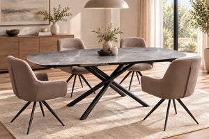 Un juego de comedor moderno que incluye una mesa ovalada de color gris oscuro con efecto piedra y base negra en forma de cruz, rodeada por cuatro sillas tapizadas en beige con patas de metal negro, todo ello sobre una alfombra clara en un comedor luminoso.