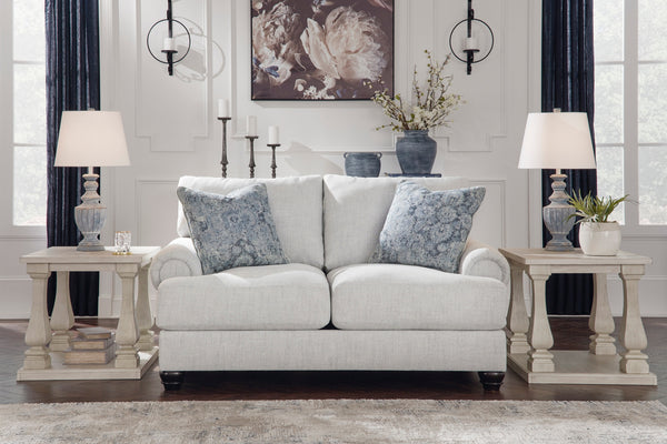 Loveseat blanco con cojines decorativos en un salón con mesas auxiliares y lámparas.