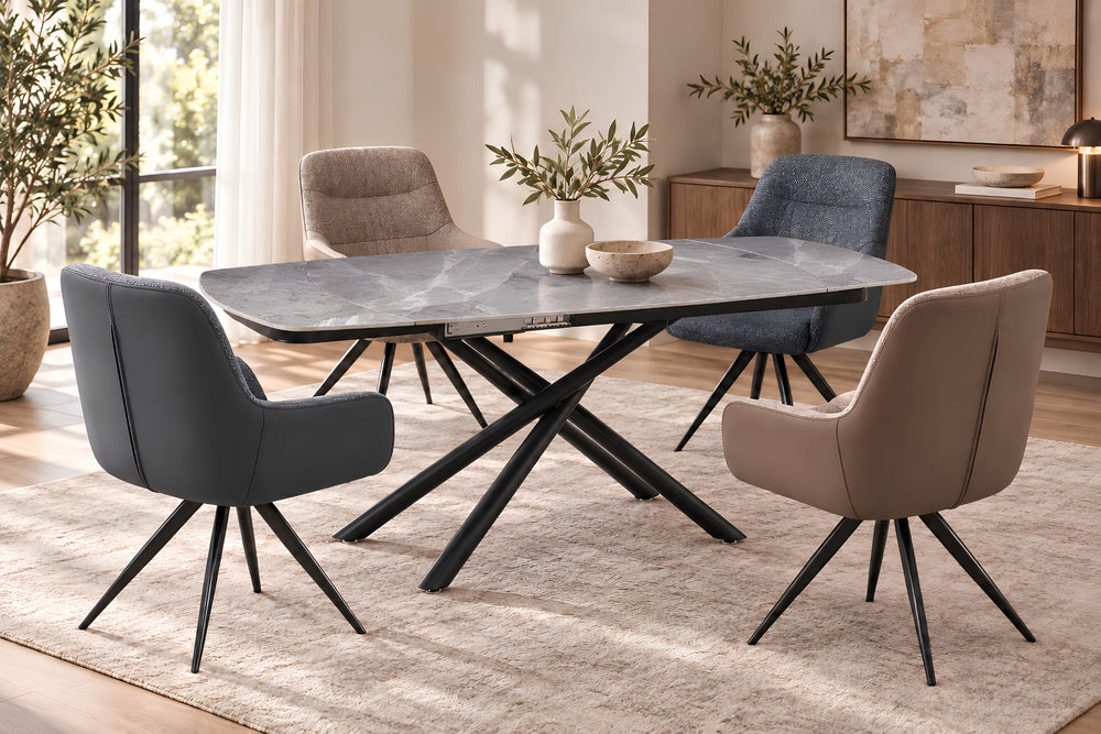Un juego de comedor moderno que incluye una mesa rectangular con acabado de piedra gris y base negra en forma de X, rodeada por cuatro sillas tapizadas en gris, beige y azul, y situada sobre una alfombra clara en un comedor luminoso.