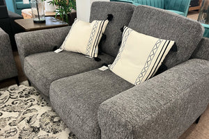 Loveseat gris con cojines decorativos en una sala de exposición