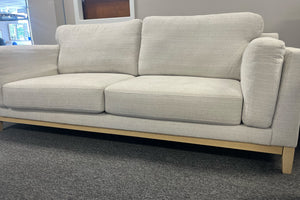 Sofá beige con patas de madera en una sala de exposición