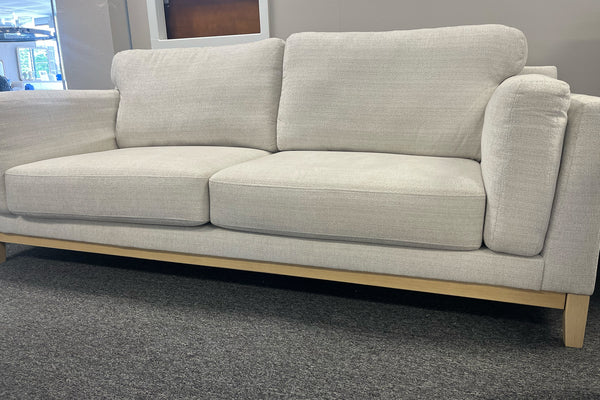 Sofá beige con patas de madera en una sala de exposición