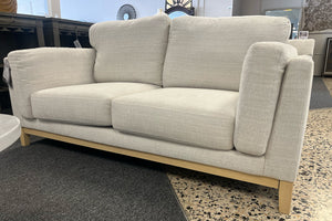 Loveseat beige con patas de madera en un entorno de exposición.