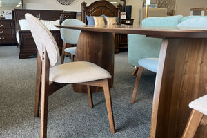 Detalle lateral de un juego de comedor contemporáneo con mesa rectangular de acabado nogal y sillas tapizadas en tonos beige y gris claro. Se aprecian las bases curvas de madera y el diseño ergonómico de las sillas, exhibidos en una tienda de muebles.