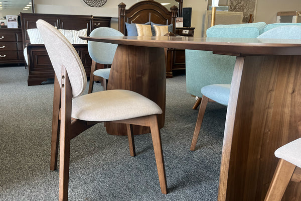 Detalle lateral de un juego de comedor contemporáneo con mesa rectangular de acabado nogal y sillas tapizadas en tonos beige y gris claro. Se aprecian las bases curvas de madera y el diseño ergonómico de las sillas, exhibidos en una tienda de muebles.